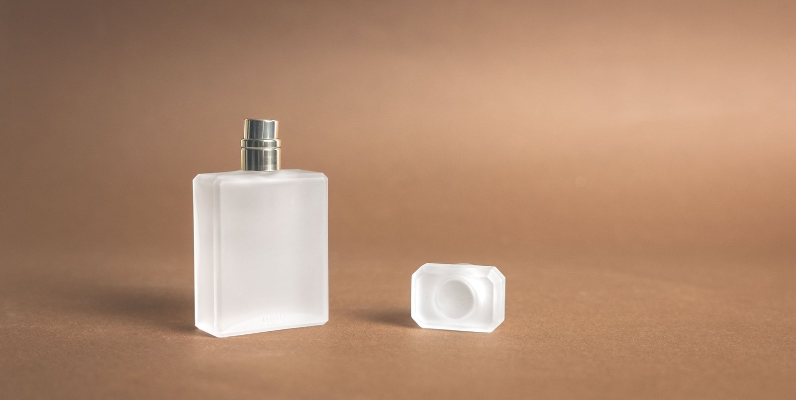 Three plain glass perfume bottles on a stone surface in soft daylight, with dried lavender and cotton stems beside them